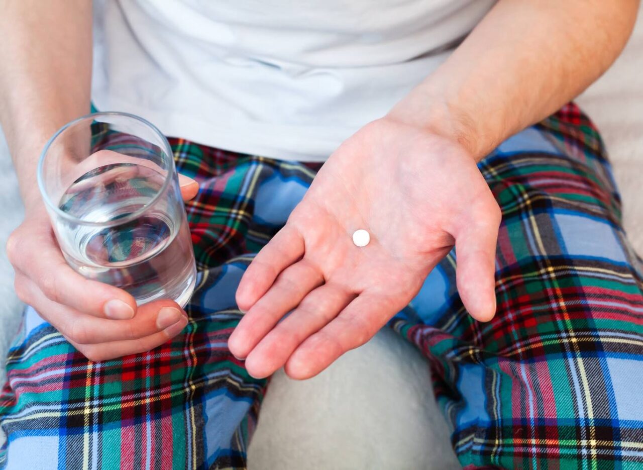 Young man holds one pill and glass of water in hands taking antidepressant medication.