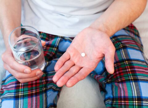 Young man holds one pill and glass of water in hands taking antidepressant medication.