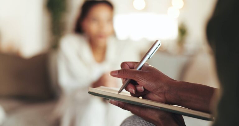 Hand of a Mental health therapist holding a pen and writing while meeting with young woman