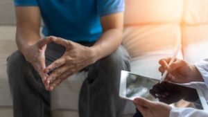 Man sits on couch, leaning forward to talk to doctor about physical symptoms of depression.